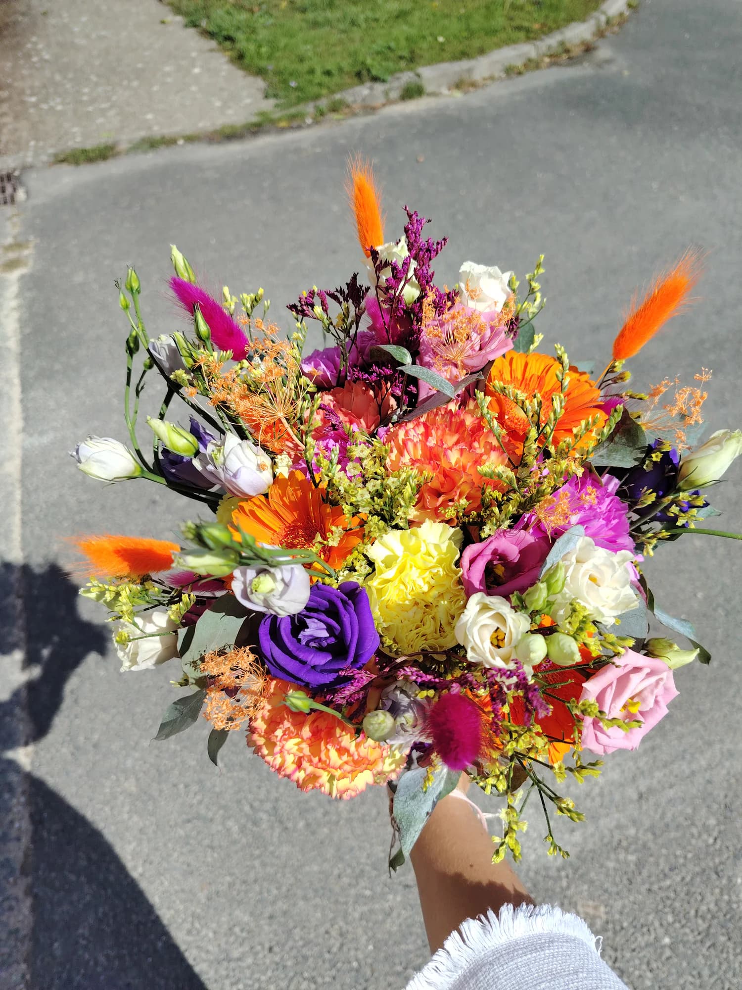 Bouquet très coloré orange, rose, violet et jaune, tenu à bout de bras en extérieur