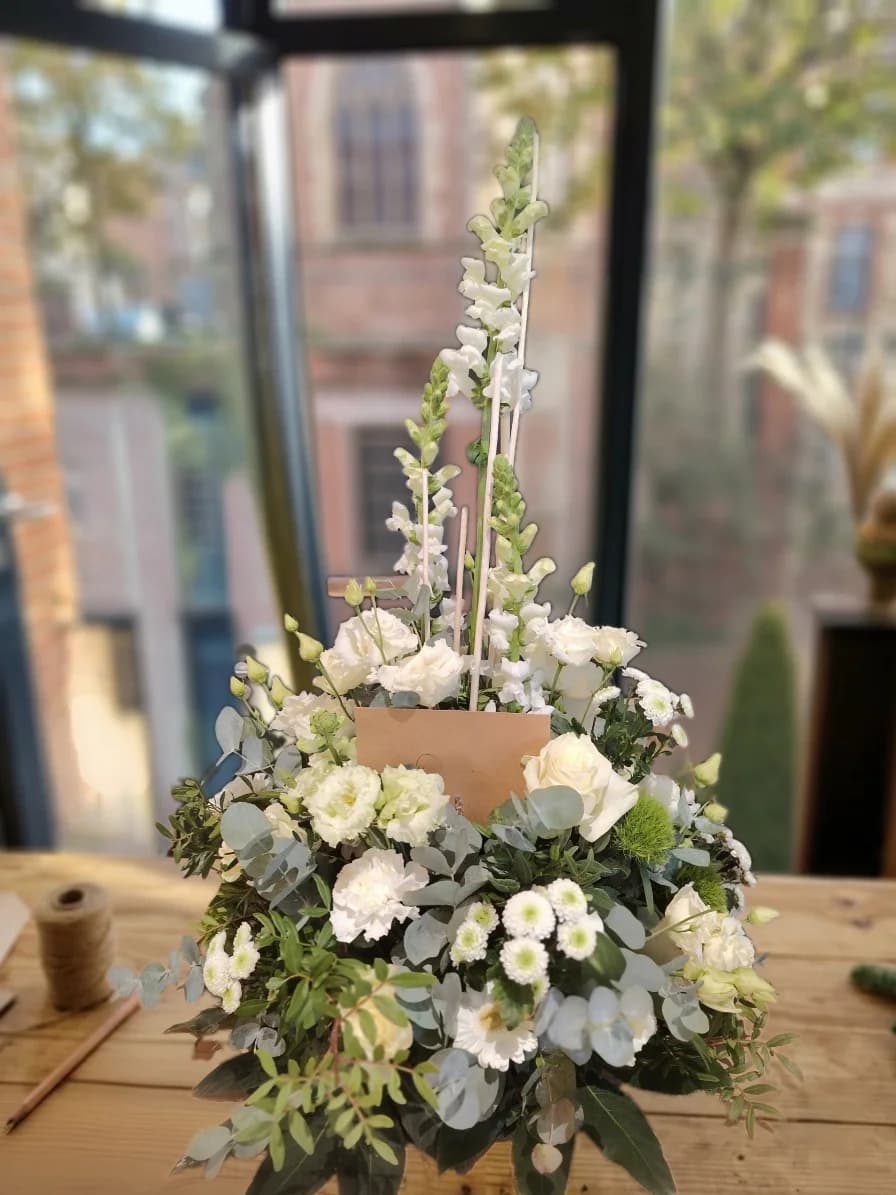 Grande composition florale blanche et verte aux tiges verticales, posée sur une table en bois